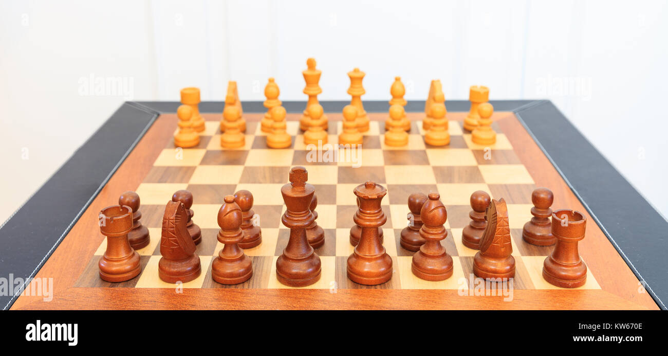 Wooden chessboard with chess pieces on it. Leather frame, close up view, details, white background. Stock Photo