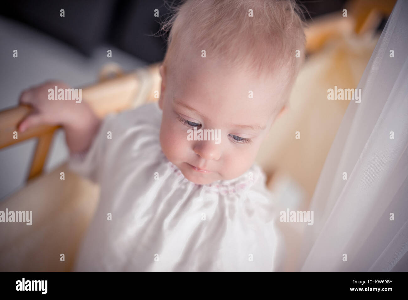 Charming baby is standsing in crib and looking down Stock Photo Alamy