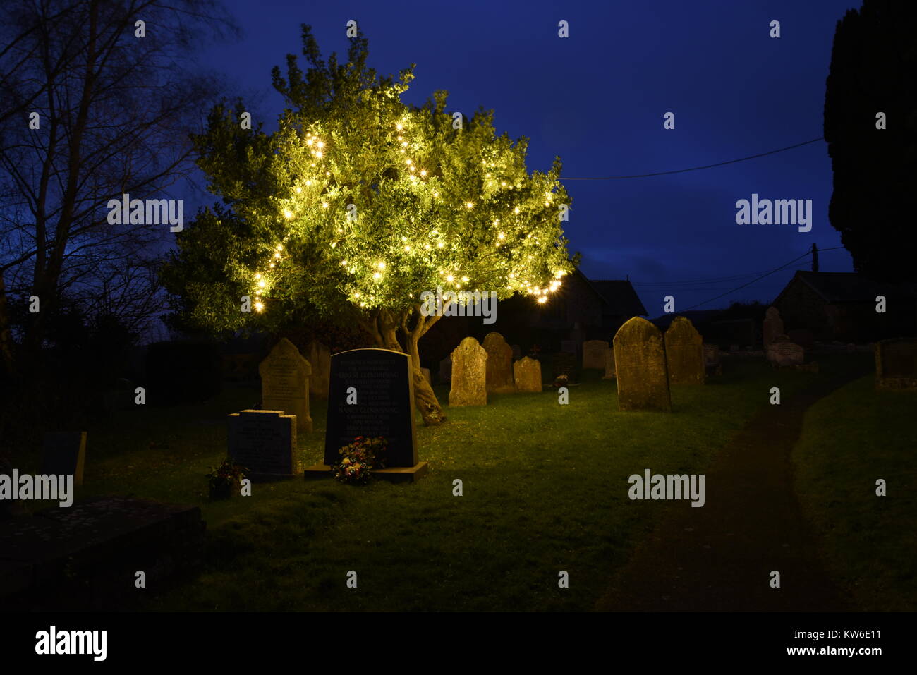 Gravestones illuminated at night in a village cemetery, Devon, England