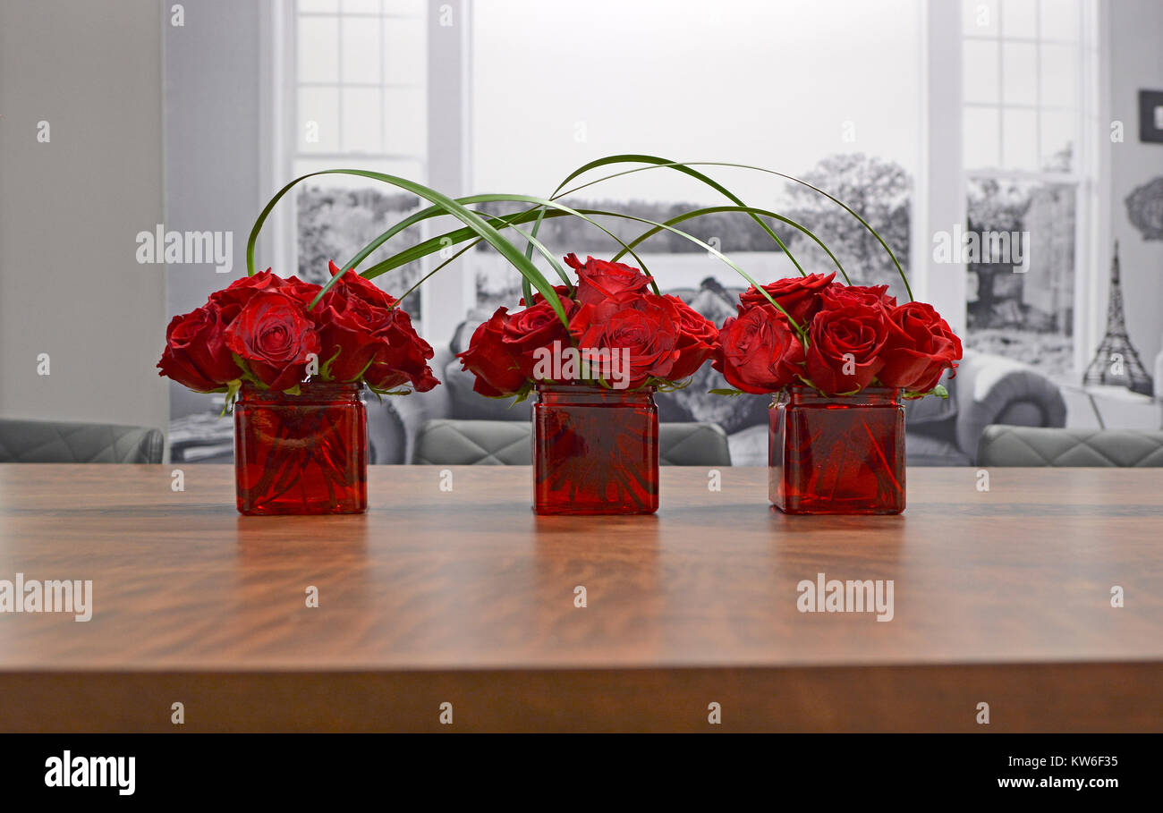 Three vases filled with red roses and joined by grasses against a black and white background