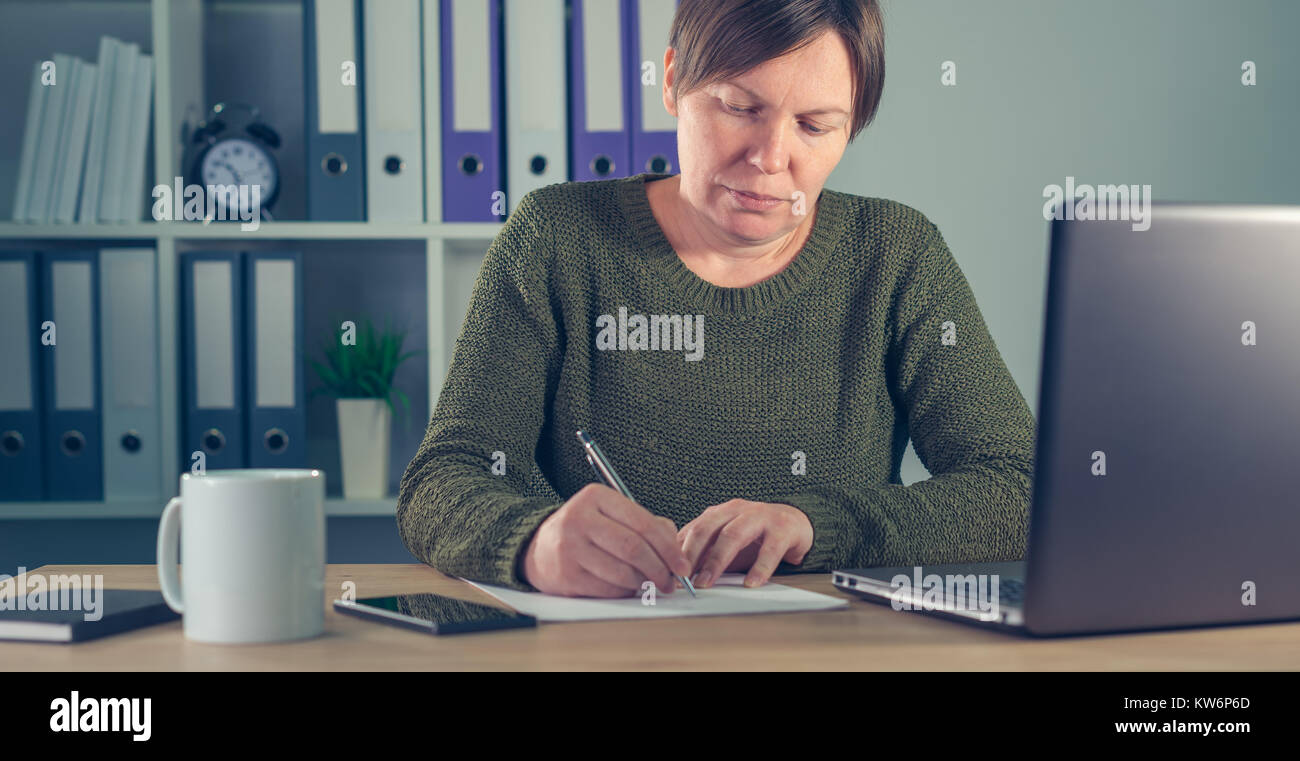 Businesswoman signing papers or writing notes in small business office interior Stock Photo