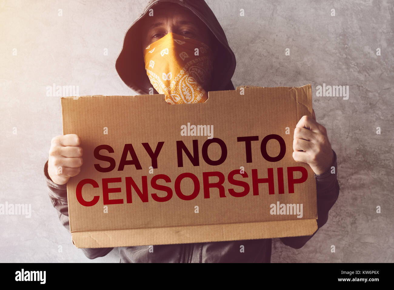 Hooded activist protestor holding Say No To Censorship protest sign. Man with hoodie and scarf over face taking part in activism and fighting for the  Stock Photo