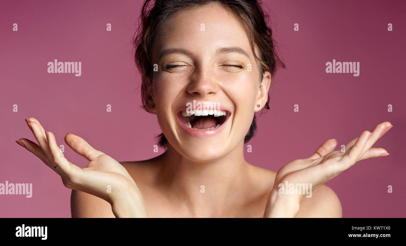 Cheerful young girl with perfect skin. Photo of brunette girl showing empty copy space on pink background. Youth and Beauty Stock Photo