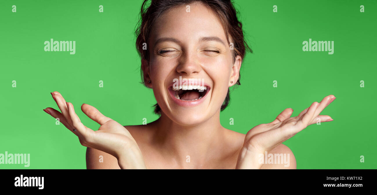 Smiling young girl with perfect skin. Photo of brunette girl showing empty copy space on green background. Youth and Beauty Stock Photo