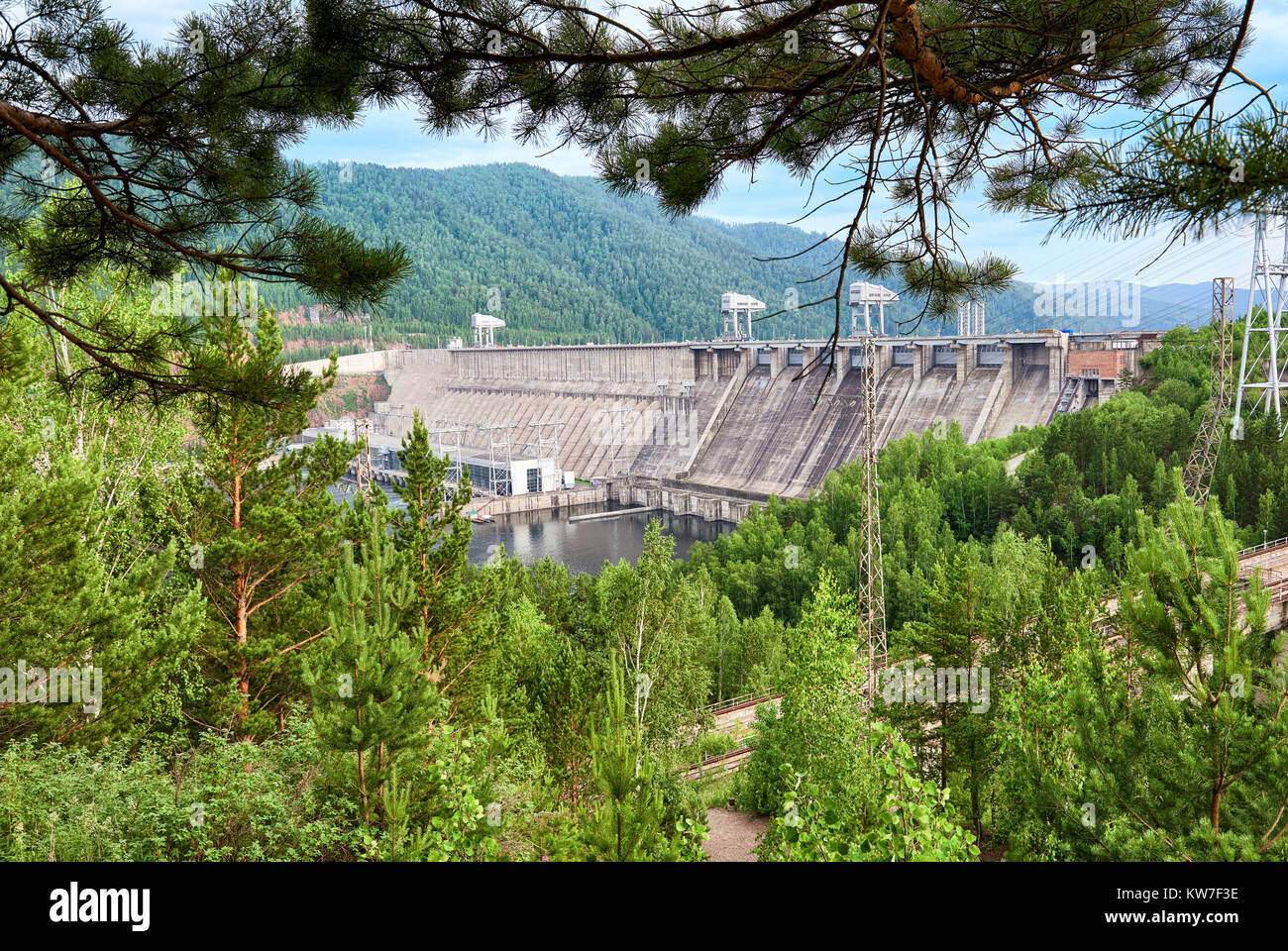 Dam is powerful Siberian hydroelectric power plant through green branches of forest. Krasnoyarsk. Eastern Siberia. Russia Stock Photo