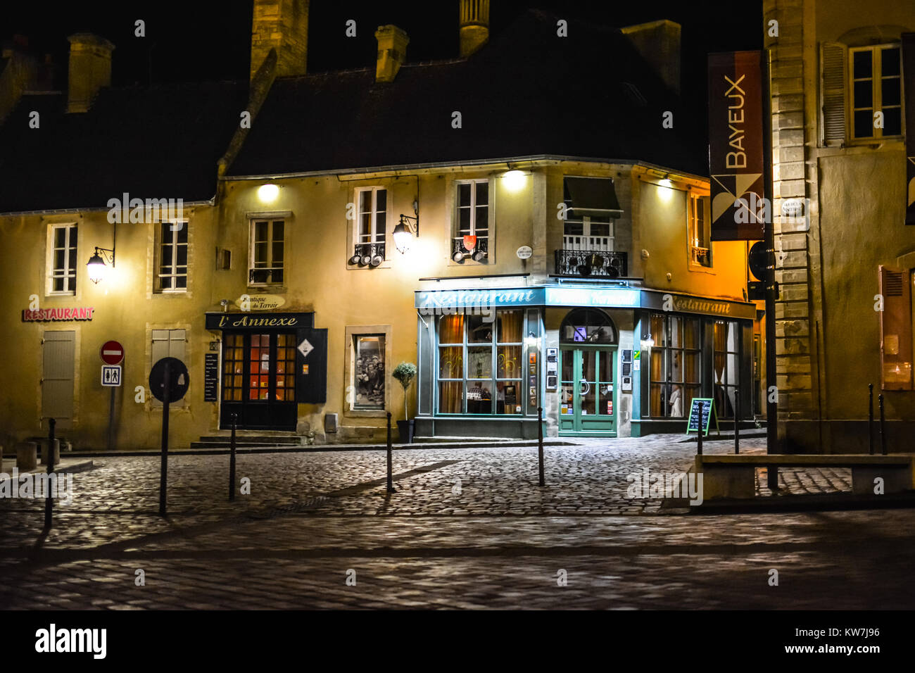 A restaurant lit up under the lights late at night on an empty street in the medieval city of Bayeux on the Normandy coast of France Stock Photo