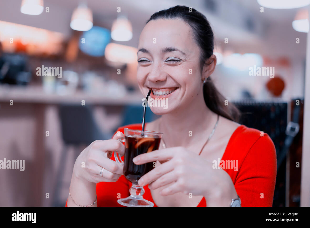 Beautiful smiling girl in red dress drinks mulled wine at coffee shop