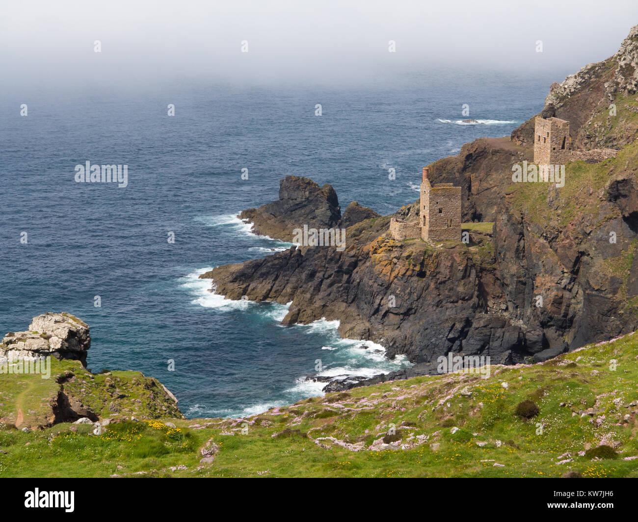 Stone buildings nestled in a cliff face looking out over the Atlantic Ocean, Cornwall Stock Photo