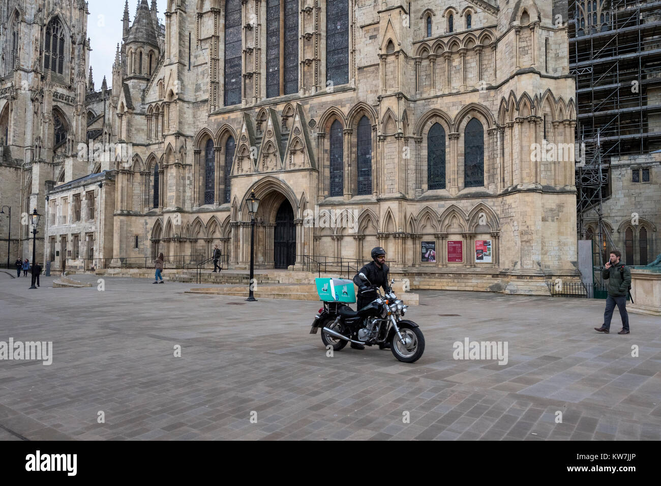 York centre - entrance to York Minster & pedestrianised piazza where people walk & Deliveroo rider pushes motorbike - North Yorkshire, England, UK. Stock Photo