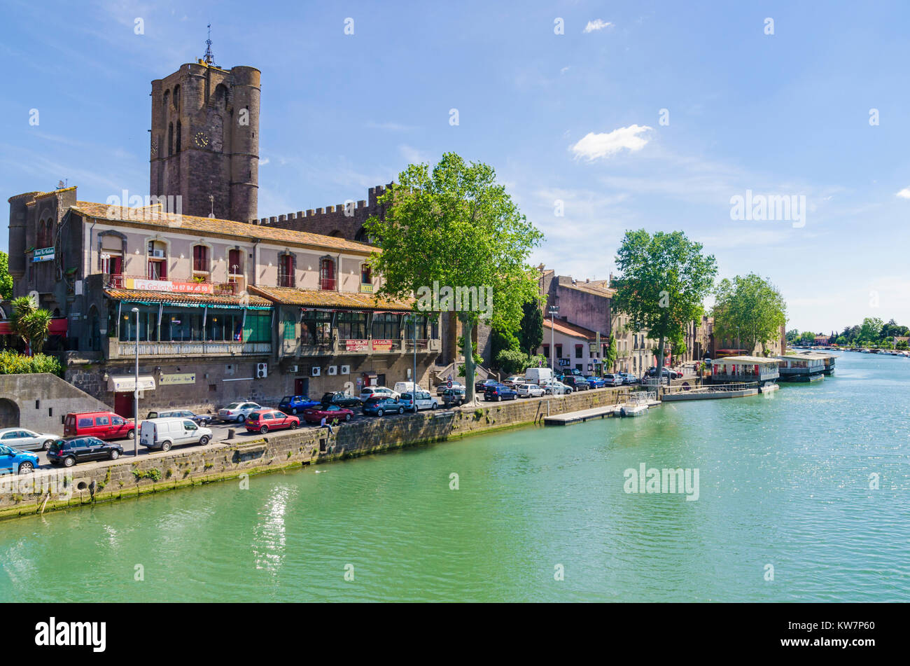 Small boats moored on the Herault River overlooked by Agde Cathedral in the town of Agde, Herault, Languedoc-Roussillon, France Stock Photo
