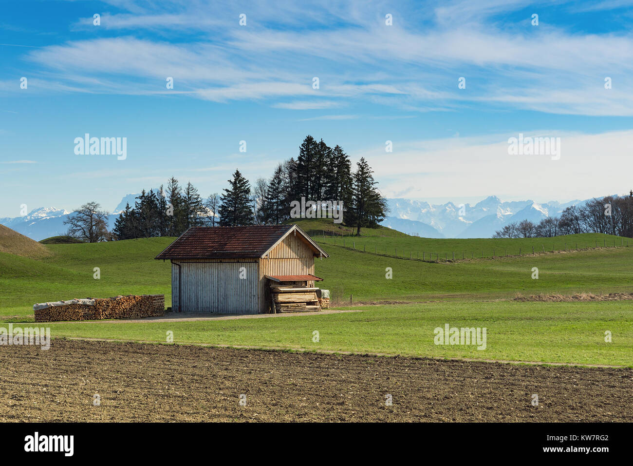 Alpine mountains spring landscape with sunny green grassland field and wooden shed Stock Photo