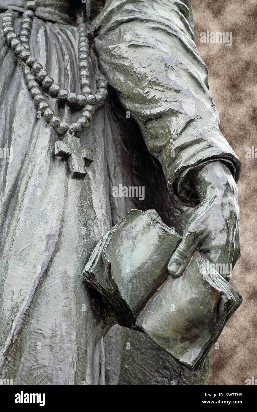 Bronze statue of a missionary priest wearing a rosary and holding a