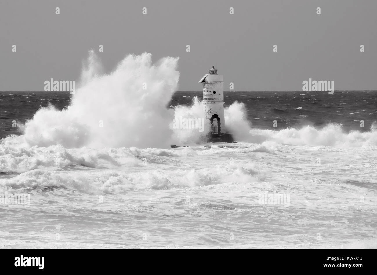 White lighthouse on the cliff. Lighthouse Mangiabarche situated in the south of Sardinia. Italy. Black and white, grey sky, white wave. Stock Photo