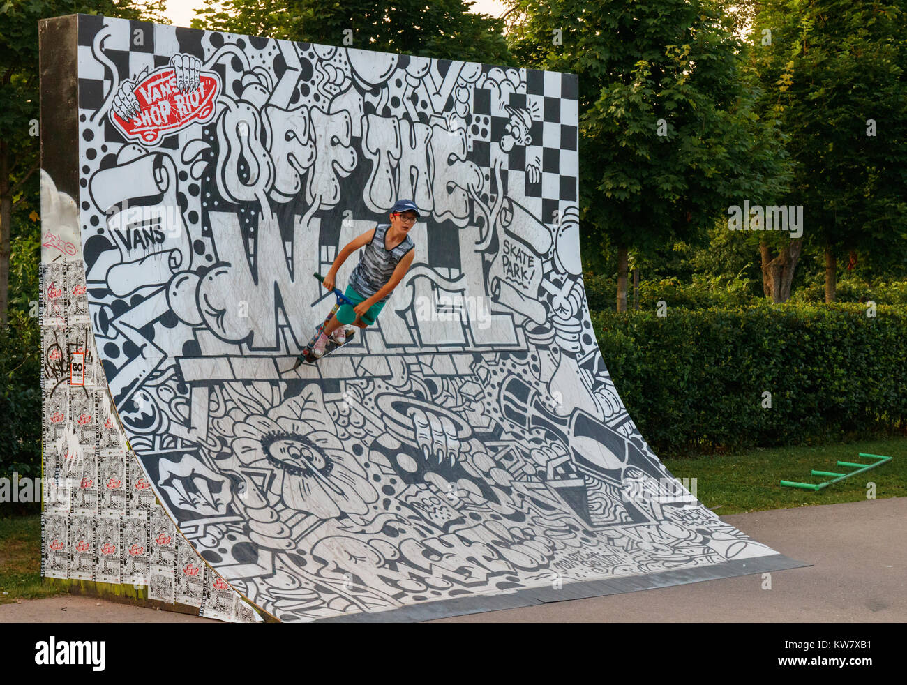 Young boy performing stunts with his kick-scooter at a ramp decorated with black and white street art in the Moscow Gorky Park, Russia. Stock Photo