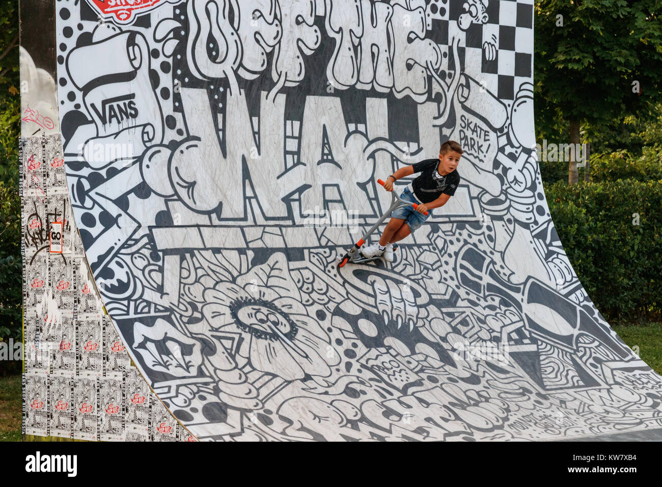 Young boy performing stunts with his kick-scooter at a ramp decorated with black and white street art in the Moscow Gorky Park, Russia. Stock Photo