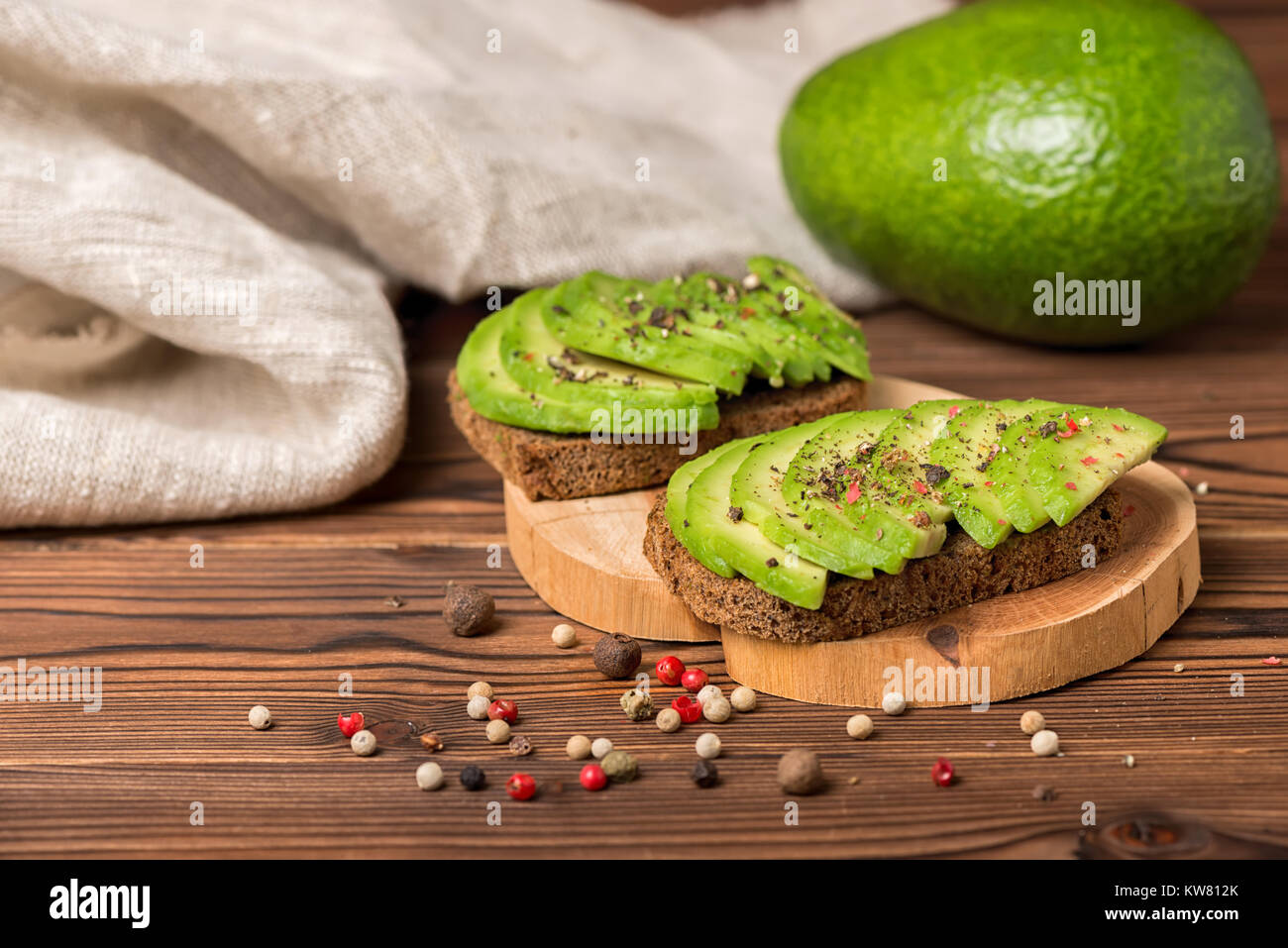 avocado sandwiches with rye bread toast and sprinkle with pepper decorated alligator pear fruit on wooden background, vegetarian food Stock Photo