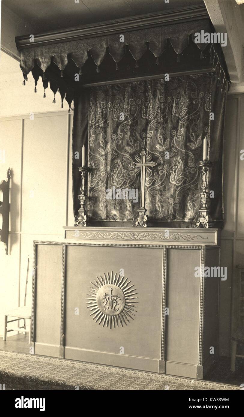 Cross between two candlesticks on an altar in a chapel with a large symbol shaped like the sun with a cross in the center of the alter at King George Military Hospital, London, England, 1915. Stock Photo