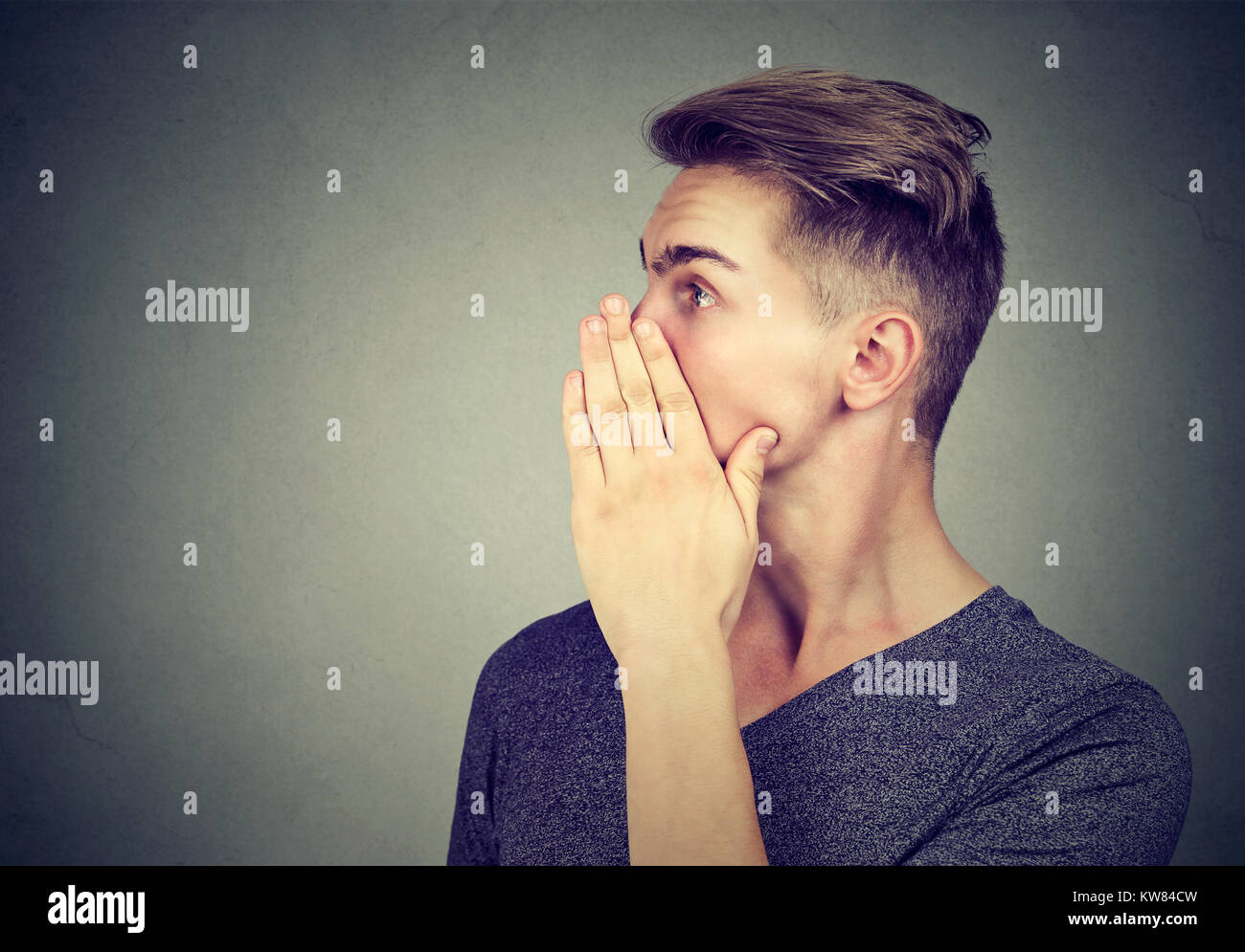 Casual young whispering while telling big secret and posing on gray backdrop. Stock Photo