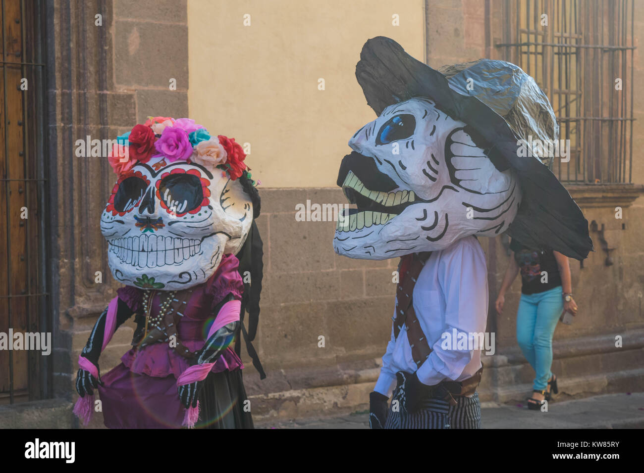 Two people in costumes including, over-size masks, hat, flowers on head and colorful clothing for the Day of the Dead party, in San Miguel de Allende Stock Photo