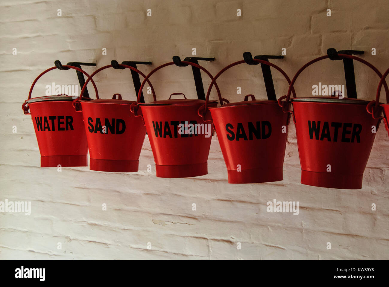 Row of red fire fighting buckets hung on a wall Stock Photo