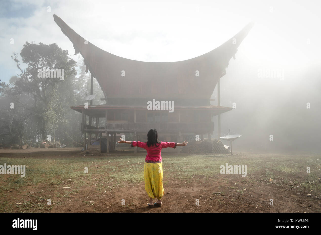 A woman standing in front of the Tongkonan house in Lolai. Lolai often known as 'Land Above the Cloud' or Negeri di Atas Awan in Banasa Indonesia. Stock Photo