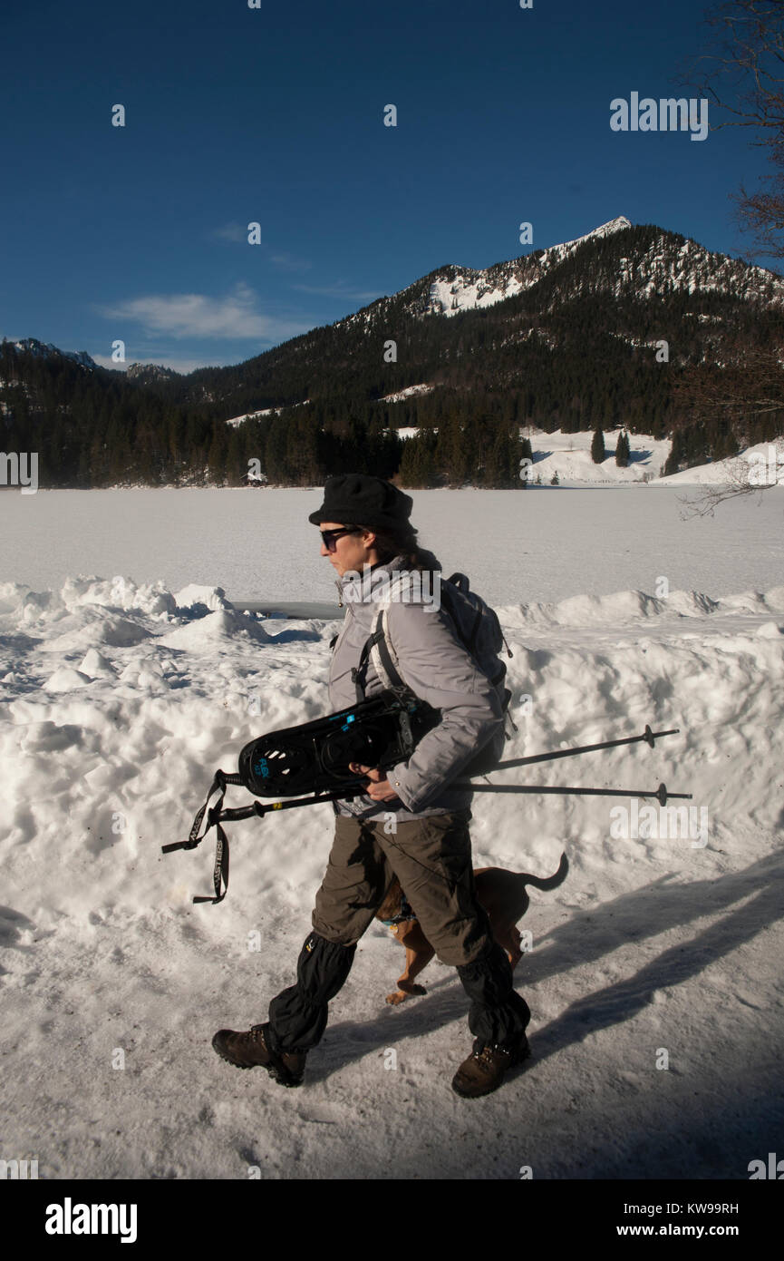 A woman equipped with canes and snowshoes walks by the Spitzingsee lake in MÃ¼nchen. Stock Photo