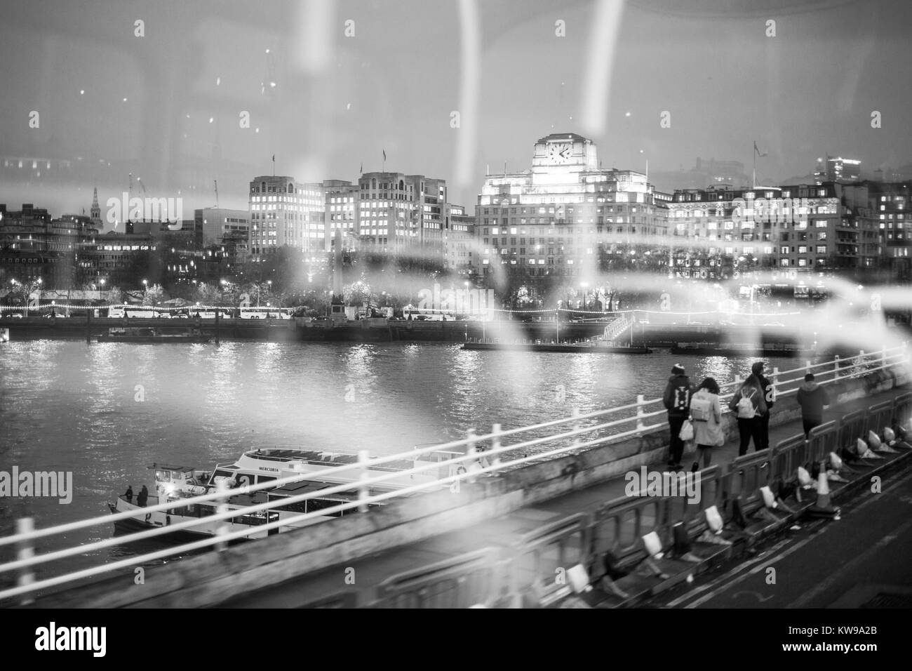 View of north bank of the River Thames in London, while crossing Waterloo Bridge, with reflection of inside of bus visible. Stock Photo