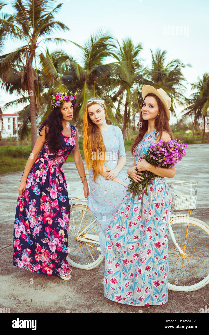 Fashion girls on vacation. Women in long dresses stand near a bicycle Stock Photo