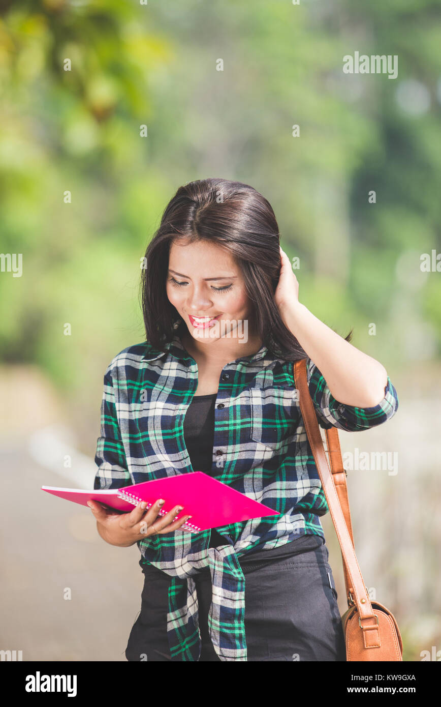 A portrait of a young asian female student holding books while walking ...