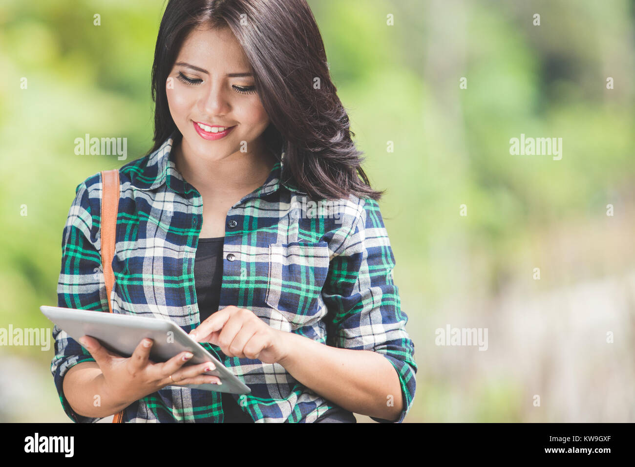 A portrait of a young asian woman using a tablet pc while walking on ...