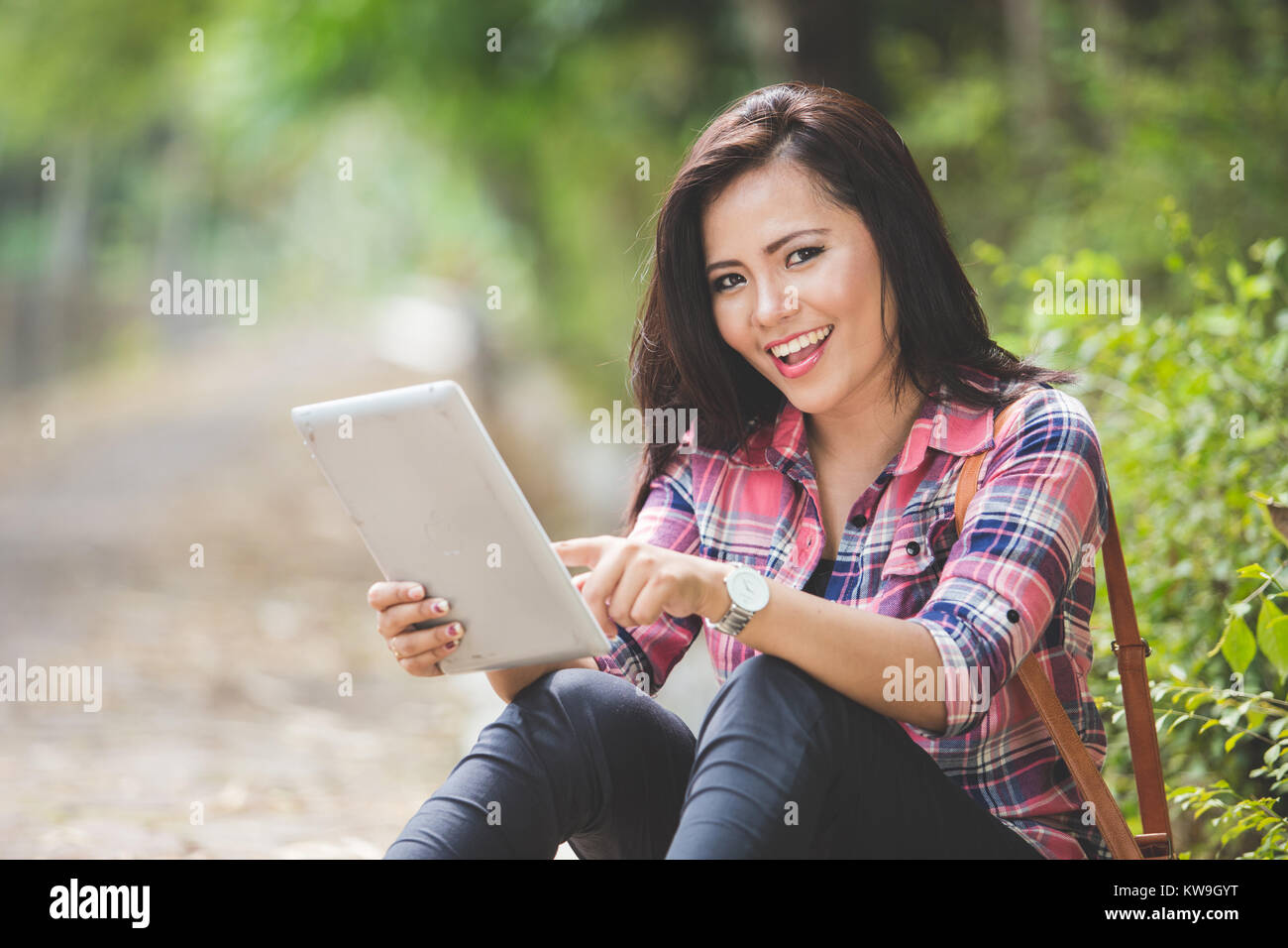 A portrait of a young asian woman holding a tablet pc while sitting on ...