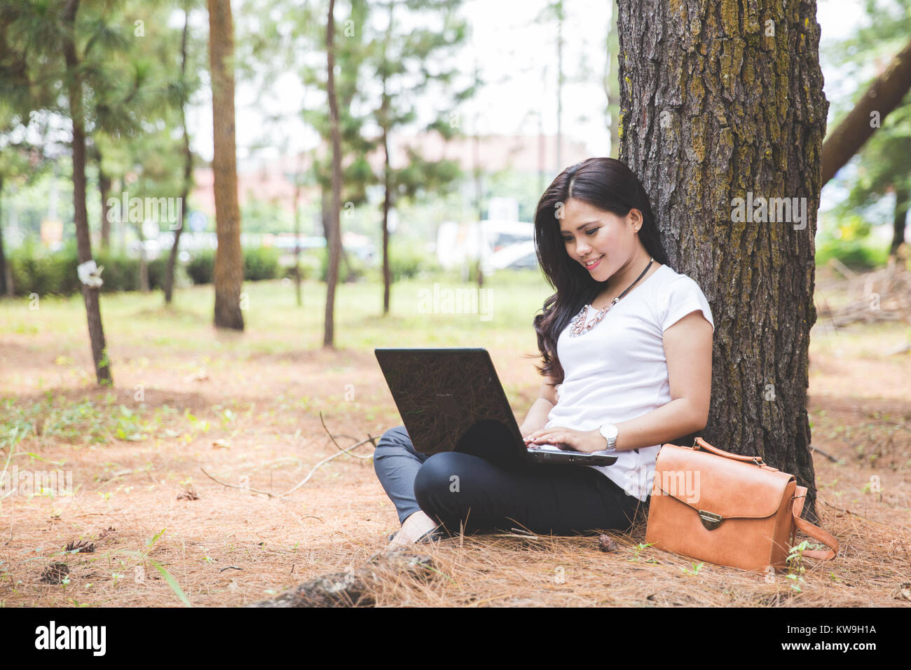 A portrait of a young asian woman using a laptop while sitting outdoor ...