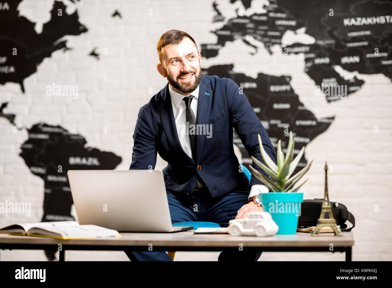 Portrait of a handsome male agent working with laptop at the travel agency office with beautiful map on the background Stock Photo
