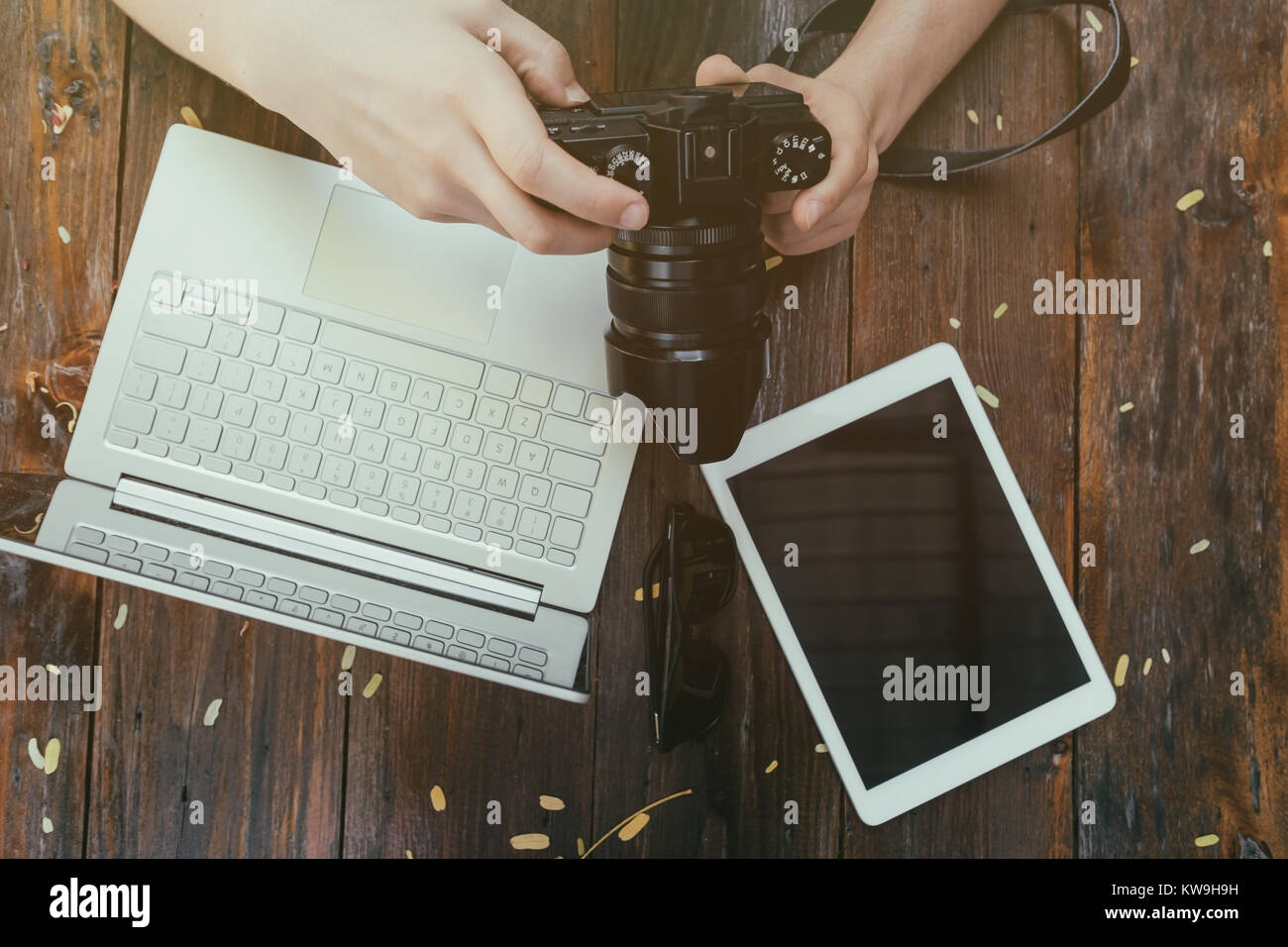 Hipster vintage wooden desktop top view, male hands holding photocamera watching photos. Laptop and tablet is on table for work Stock Photo