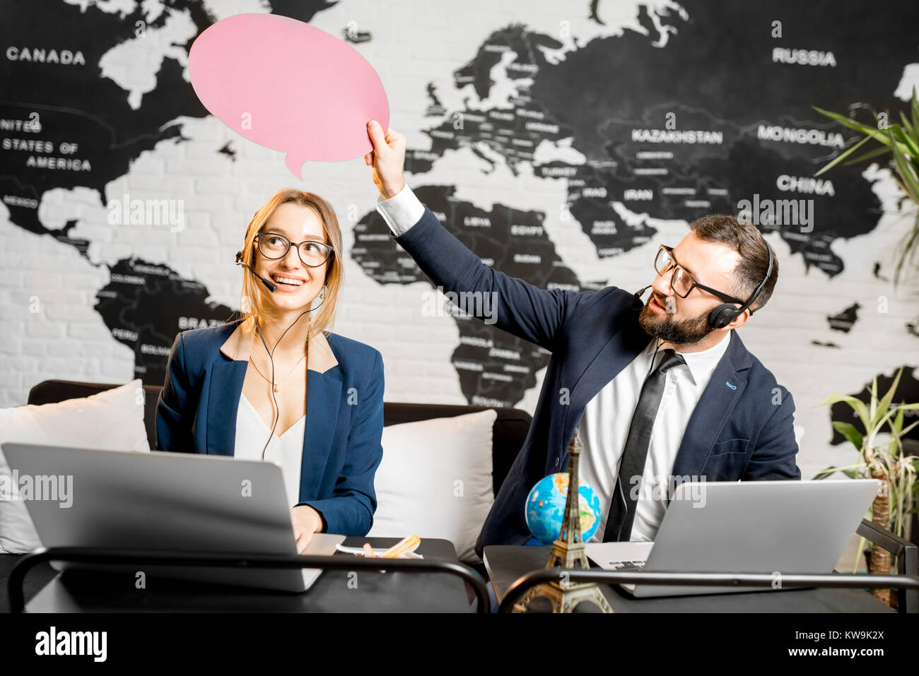 Couple of travel managers dreaming with colorful bubbles above the head sitting at the agency office with world map on the background Stock Photo