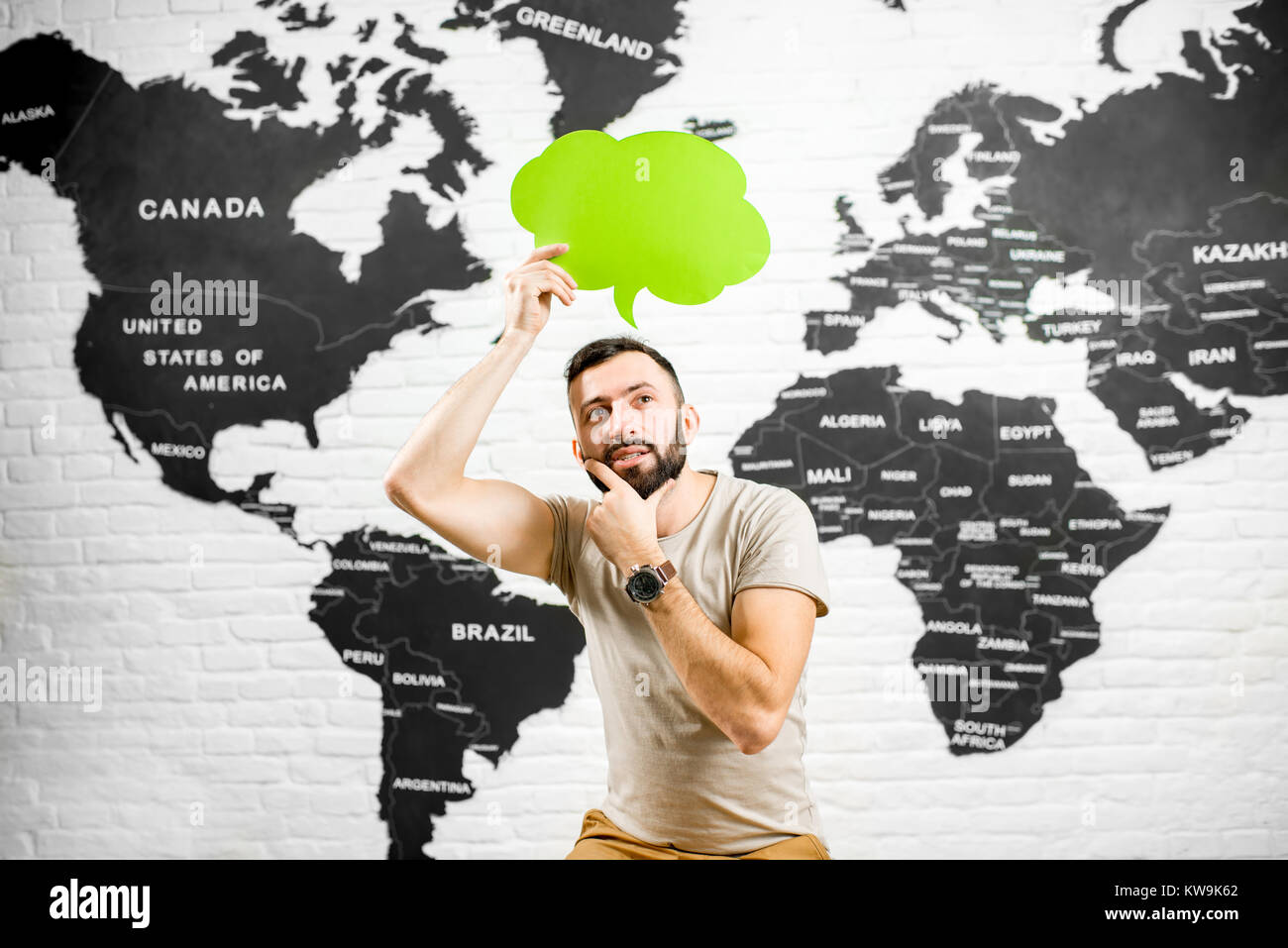 Man holding a colorful bubble above the head sitting at the office with world map on the background dreaming about traveling Stock Photo