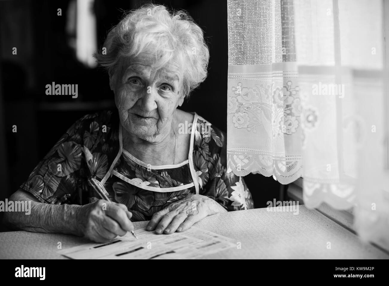 An elderly woman fills a receipt for payment of utility bills. Stock Photo