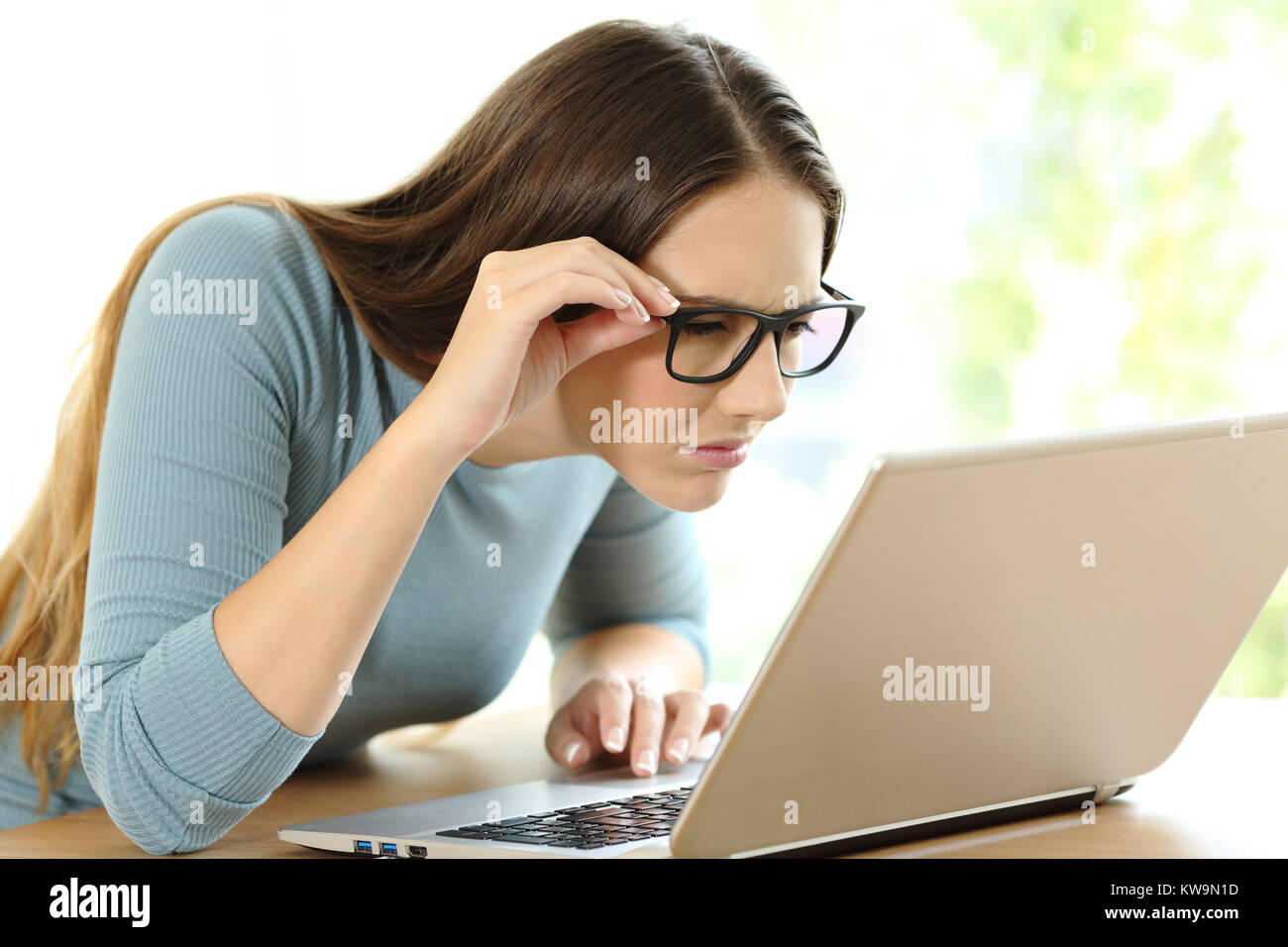 Woman with eyesight problems trying to read on line content in a laptop at home Stock Photo