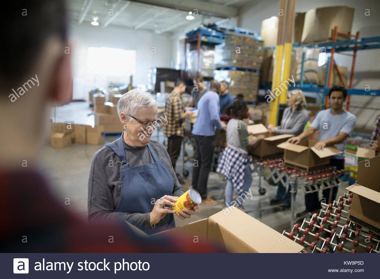 Senior woman filling donation boxes with canned food for food drive in warehouse Stock Photo