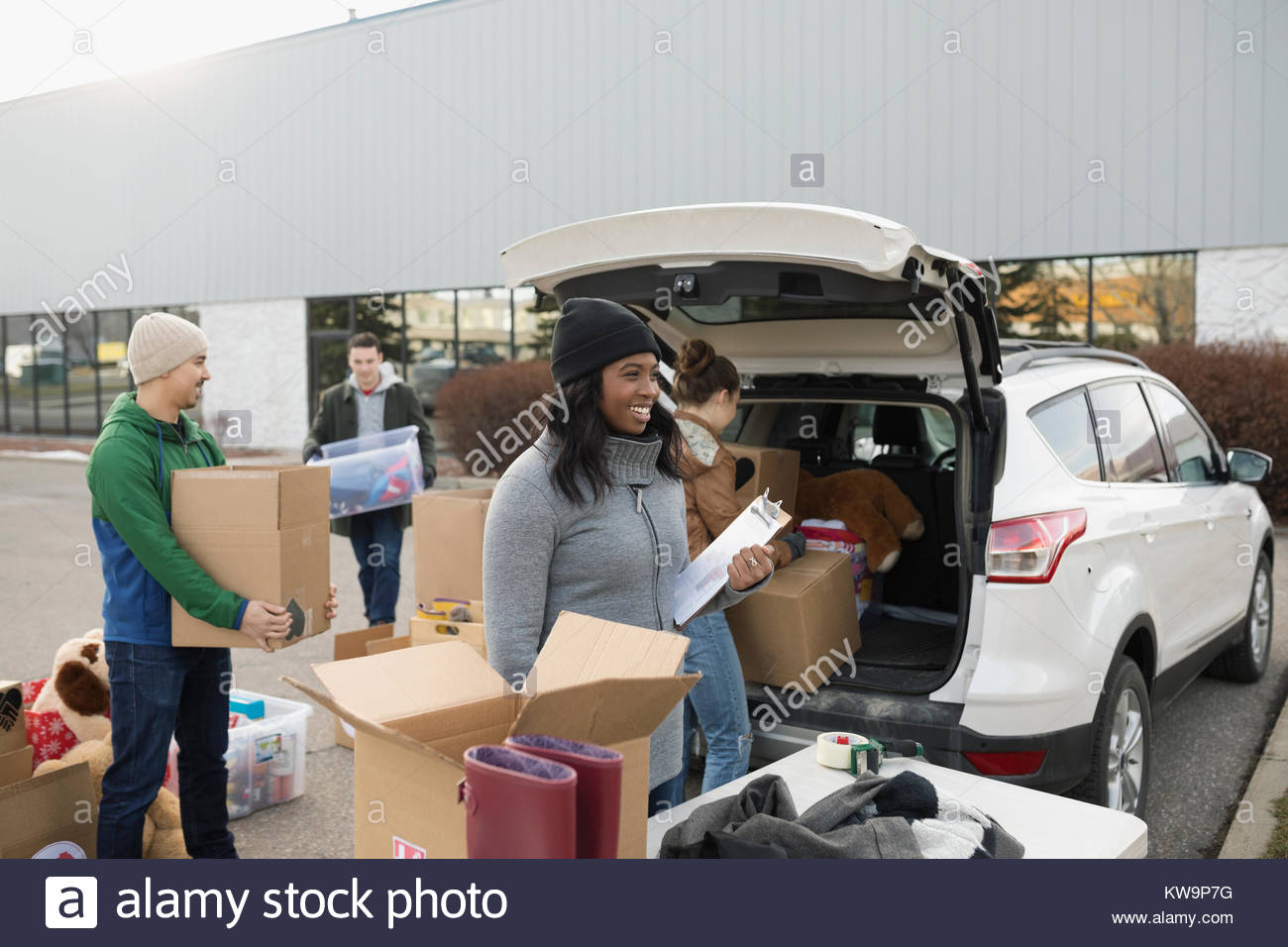 Young adult volunteers loading donation boxes into car in parking lot