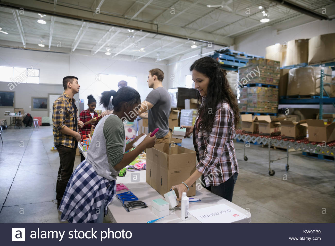 Woman and girl volunteer filling donation box in warehouse Stock Photo