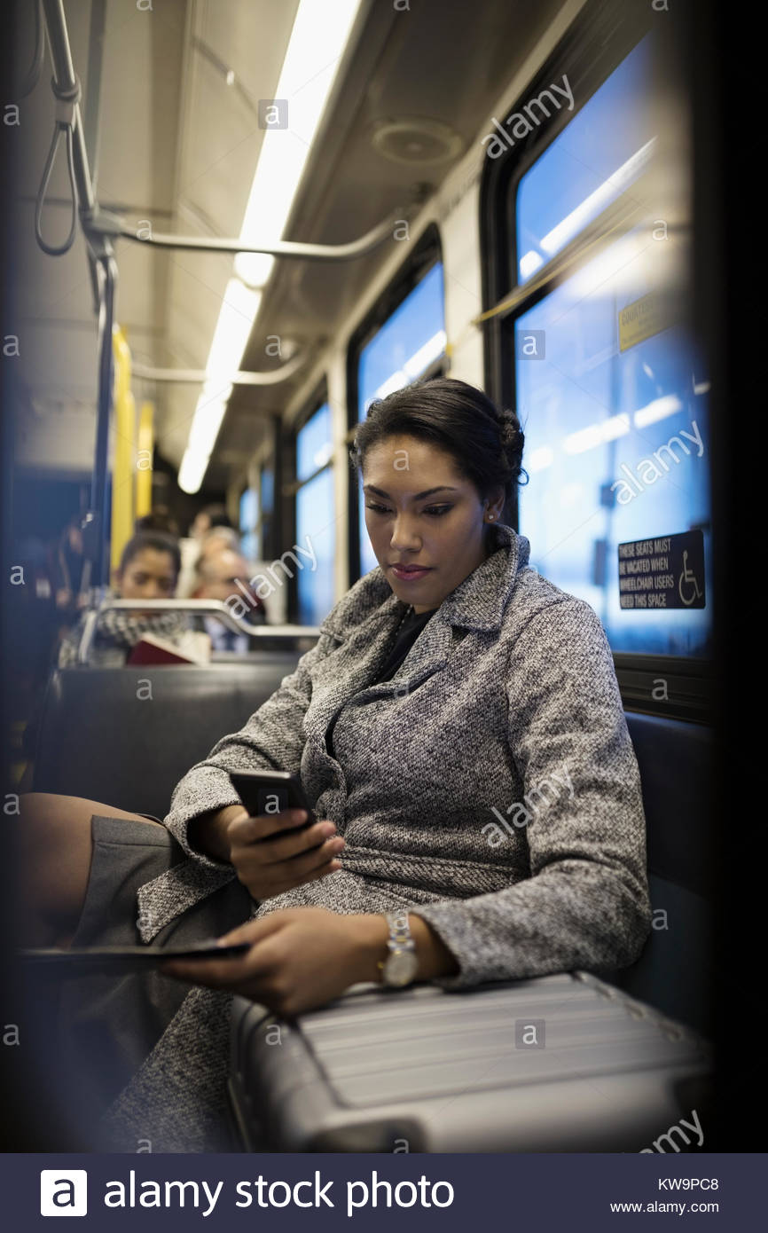 Businesswoman commuter with suitcase texting with smart phone on bus Stock Photo