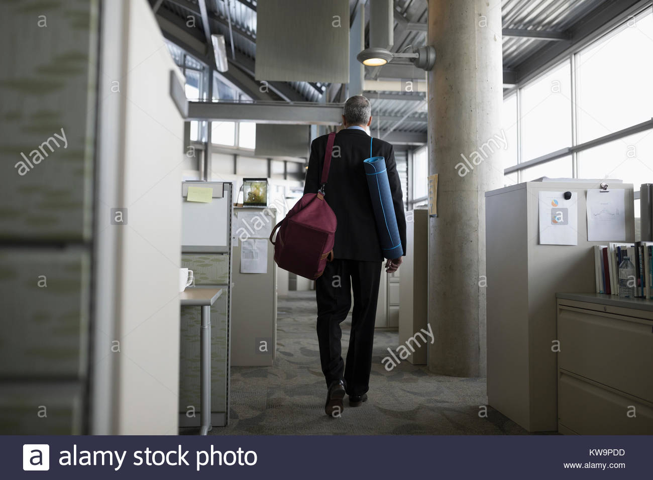 Businessman leaving office with gym bag and yoga mat Stock Photo