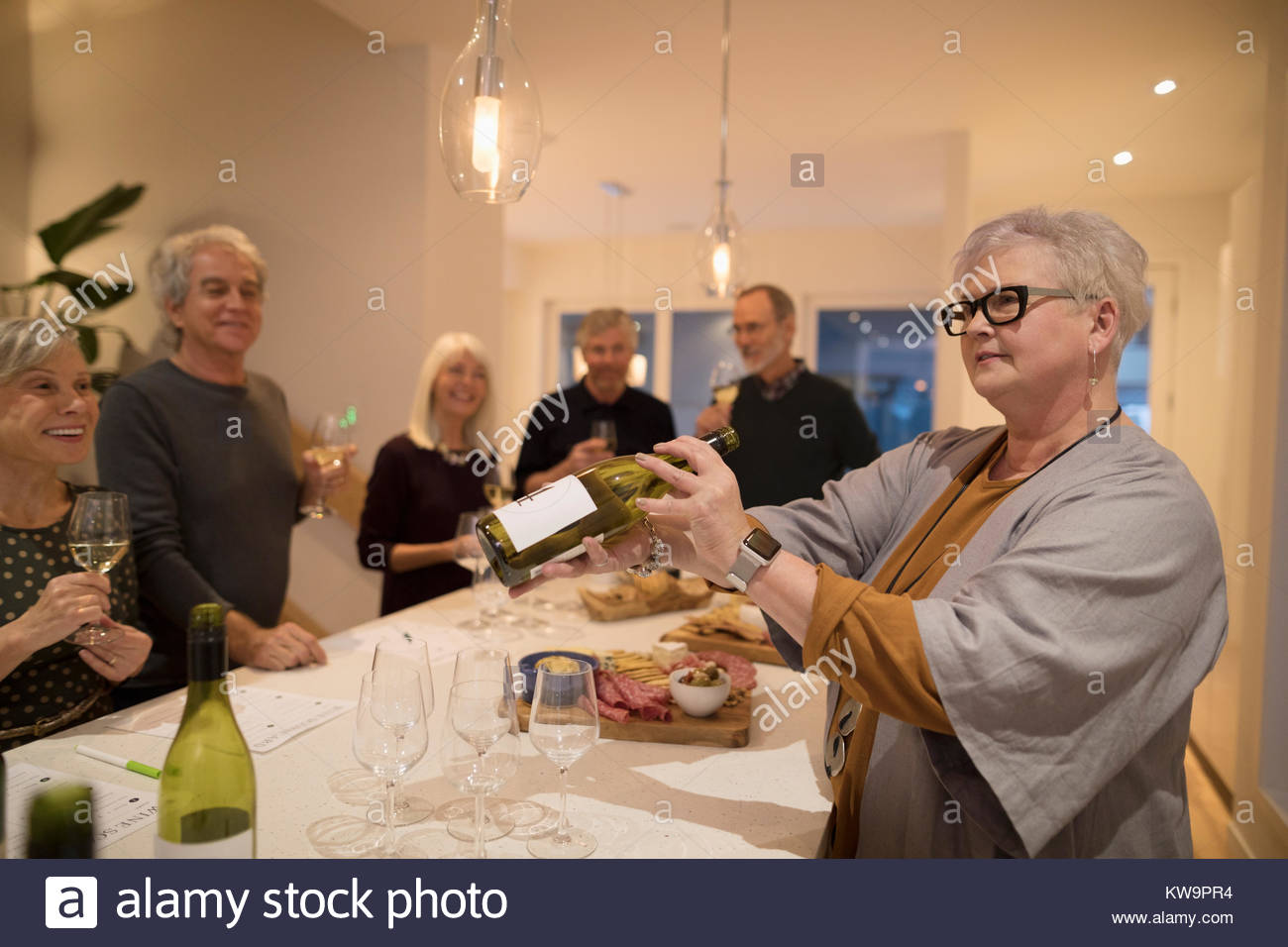 Senior woman hosting wine tasting party,showing wine bottle at dining table Stock Photo