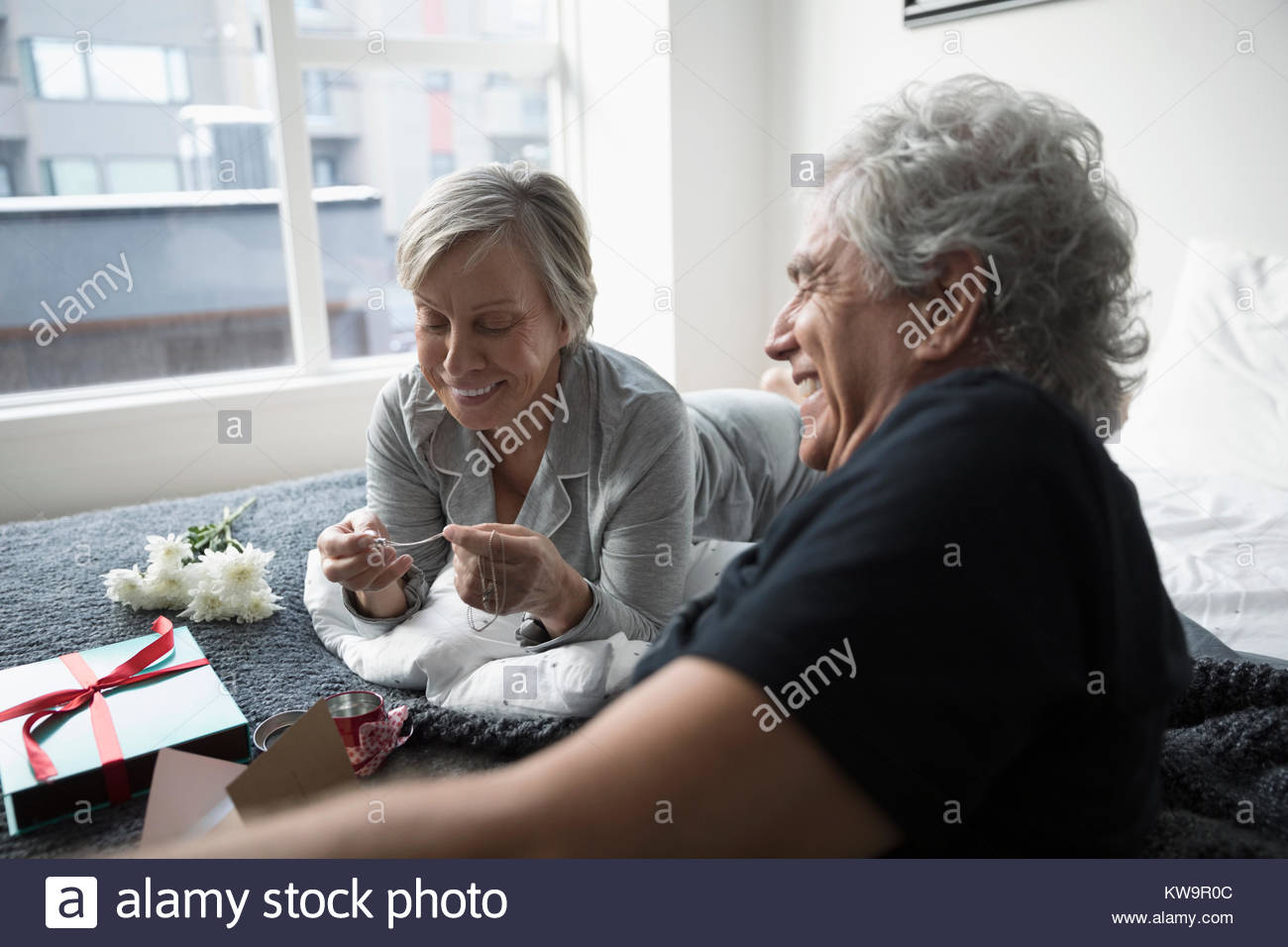 Happy senior couple in pajamas opening Valentines Day on bed Stock Photo