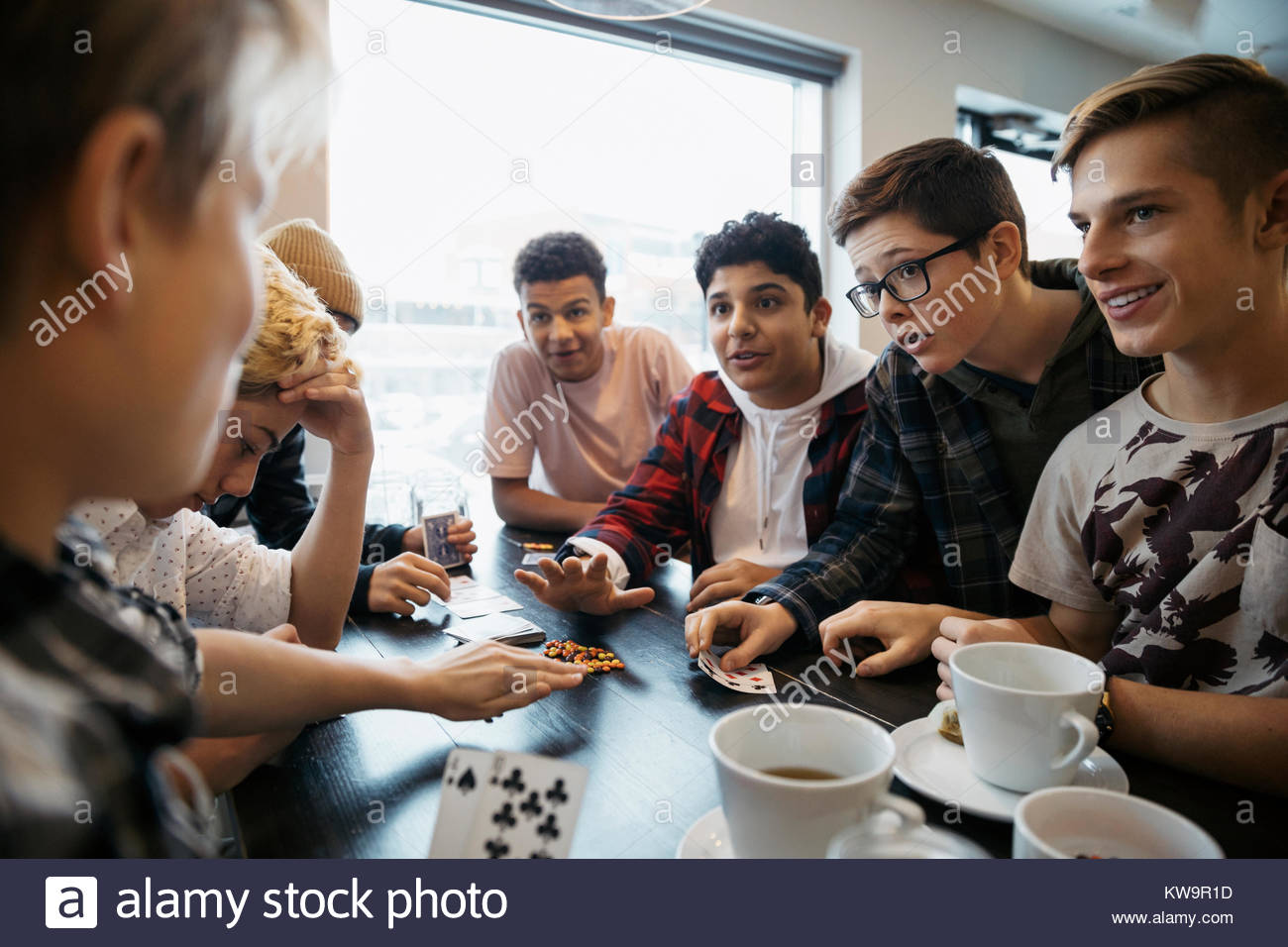 Tween boy friends playing cards and drinking coffee at cafe table Stock Photo