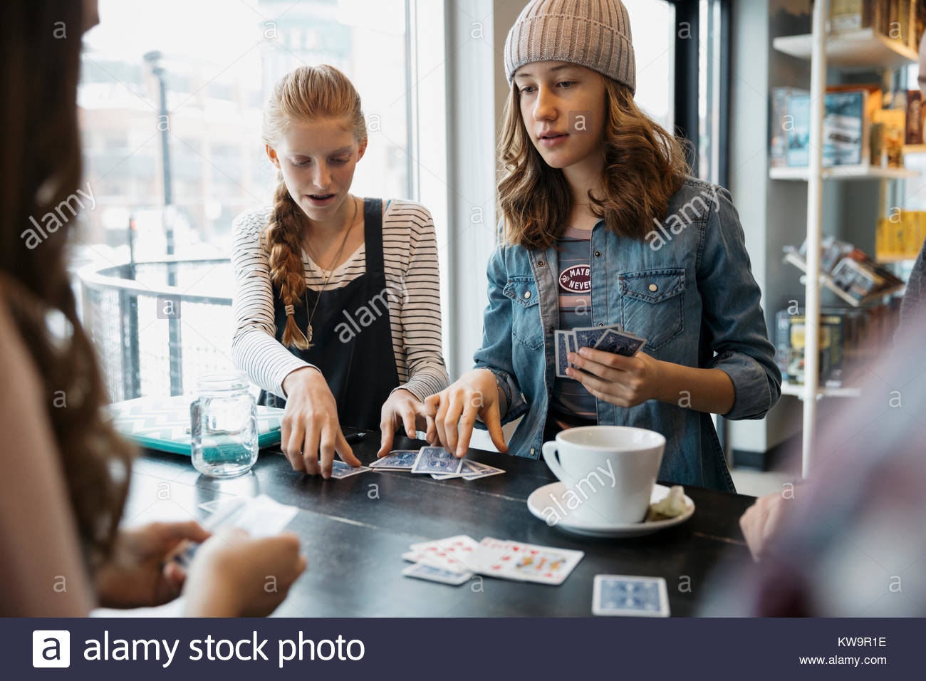 Tween girl friends playing cards and drinking coffee at cafe table Stock Photo