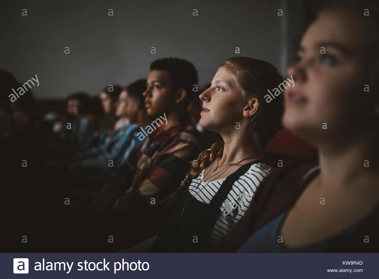 Serious tween girl watching movie in dark movie theater Stock Photo
