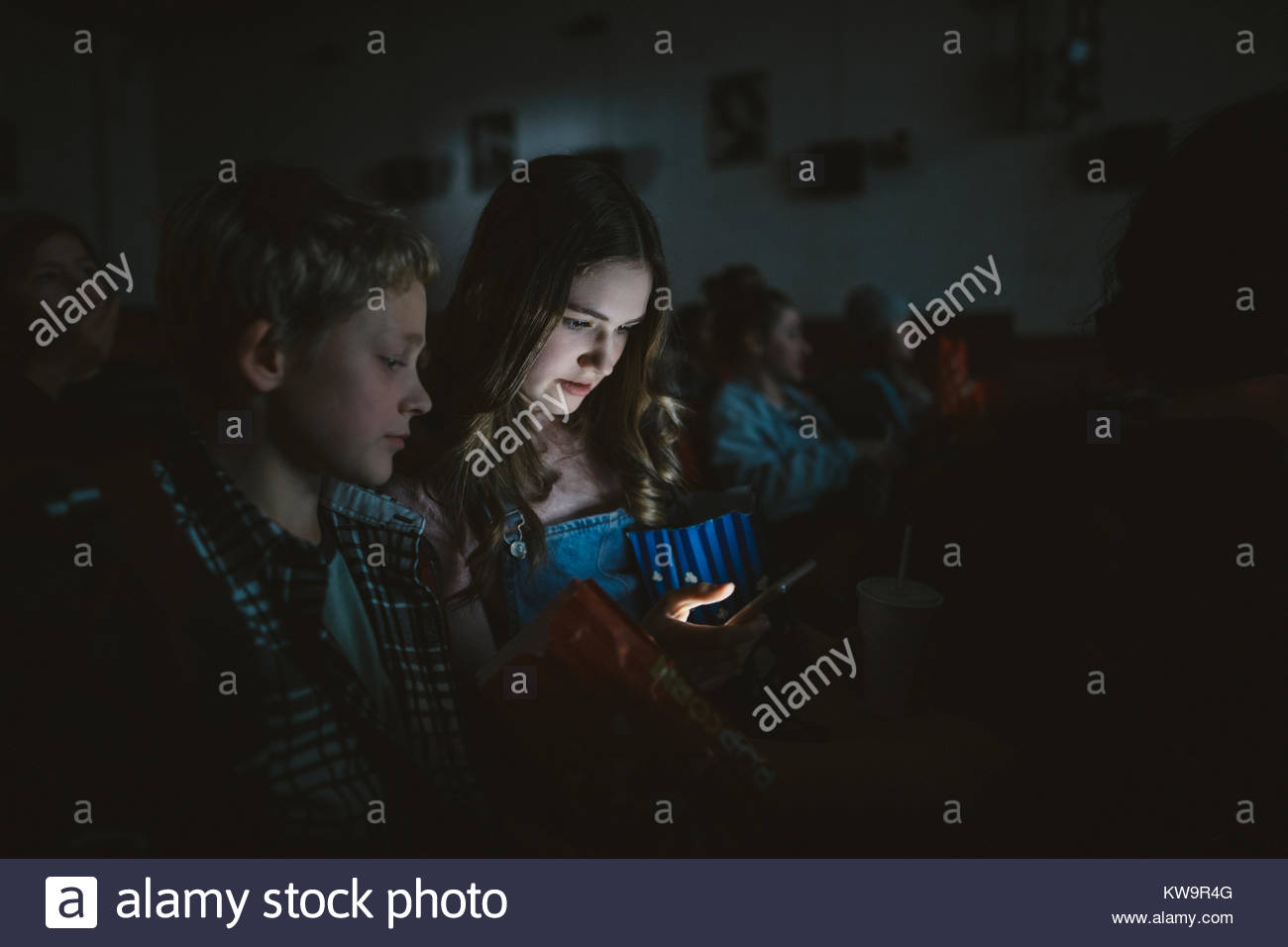 Tween girl texting with smart phone in dark movie theater Stock Photo