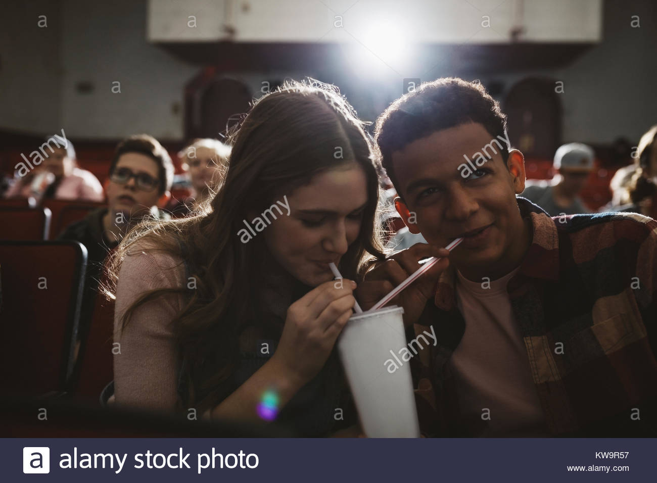 Tween couple watching movie,sharing soda with straws in dark movie